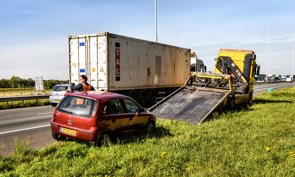 Een bergingsdienst staat bij een rode auto die niet meer verder kan rijden.